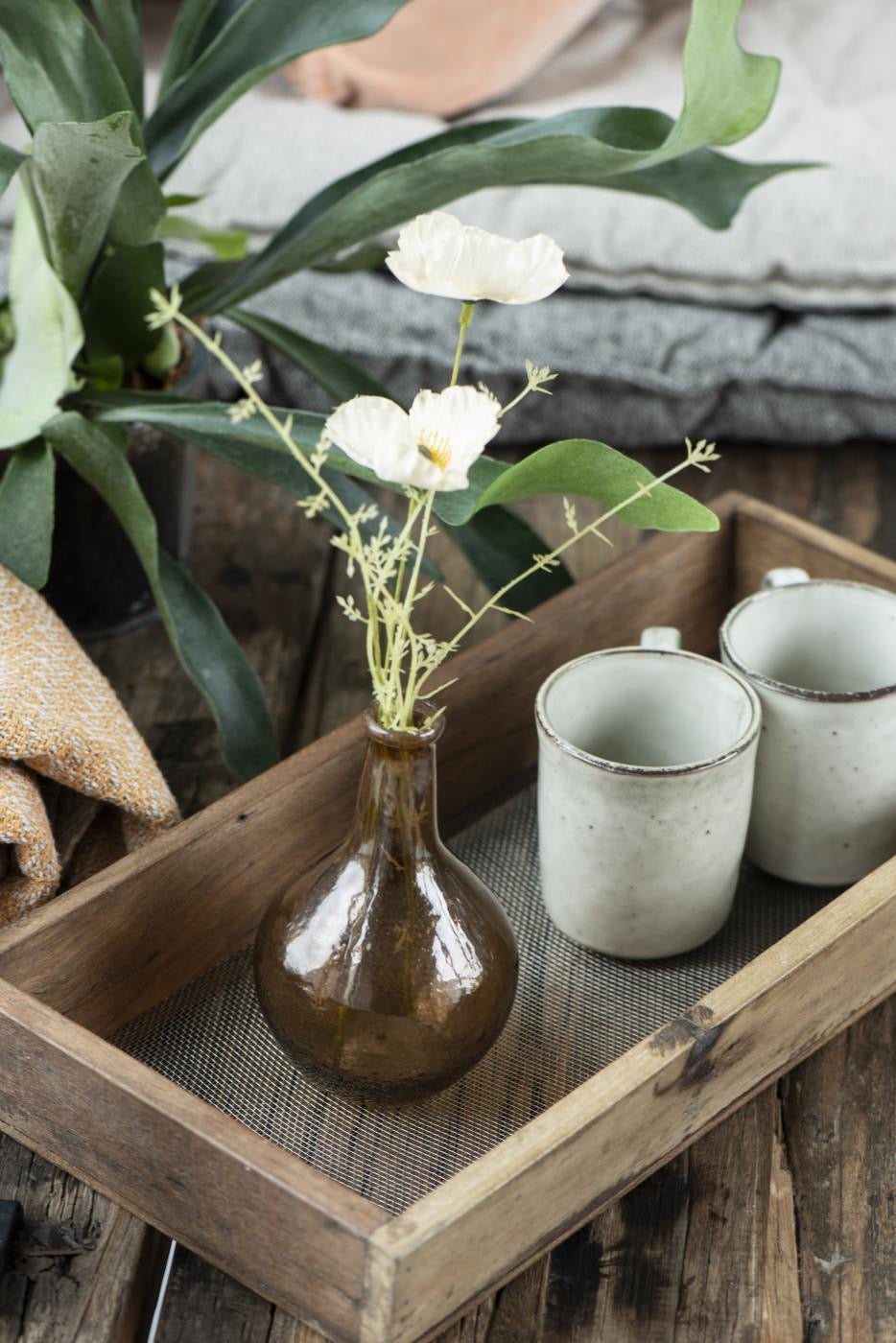 A wooden tray displaying a glass bud vase and two rustic mugs in the shade sand.