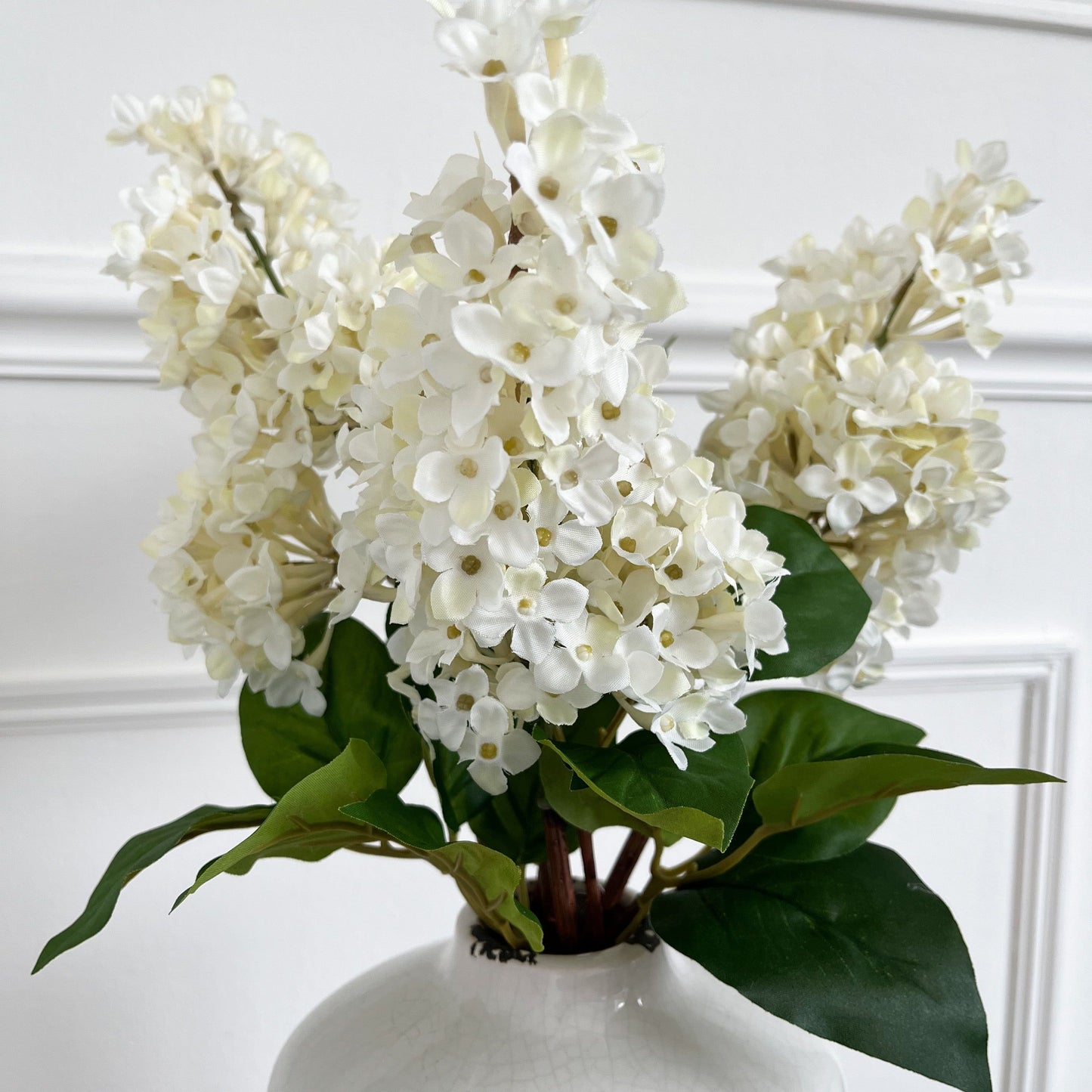 a display of 3 cream faux lilac stems displayed in a rustic cream vase