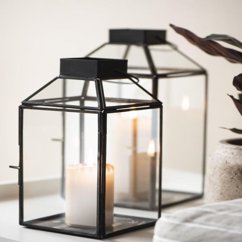 two glass and metal lanterns with black frames styled with pillar candles