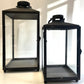 Two black lanterns with glass panels on a white background