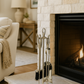 Silver fireplace tool set on a stone hearth with a lit fireplace in the background.