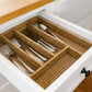Open drawer with woven silverware organizer containing forks, knives, and spoons.