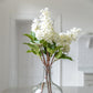 display of white artificial lilac stems in clear vase