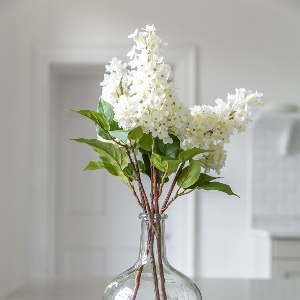 display of white artificial lilac stems in clear vase